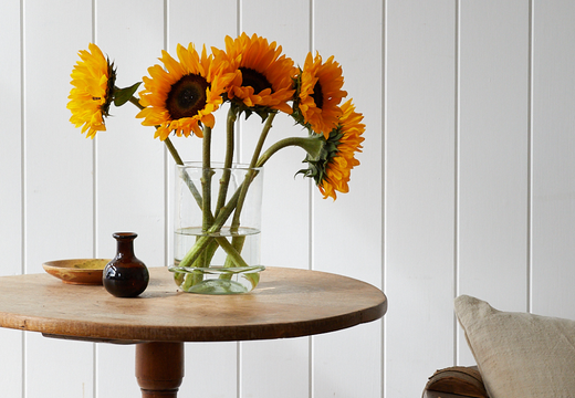 a vintage round wooden table with a La Soufflerie hand blown vase with sunflowers