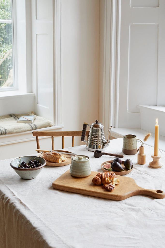a breakfast table with stainless steel kettle, leach pottery ceramics, selwyn house wooden ware and beeswax candles serving coffee and croissants