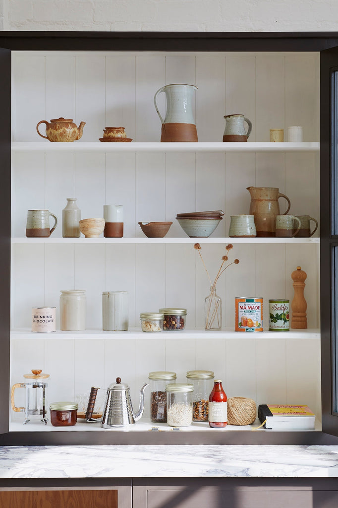 a large kitchen cupboard with pantry items, ceramics and screw top jars