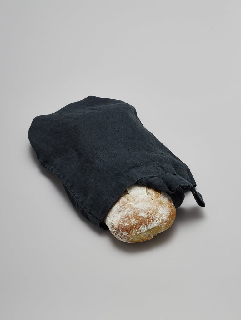 Handmade natural linen bread bag in charcoal holding a loaf of bread
